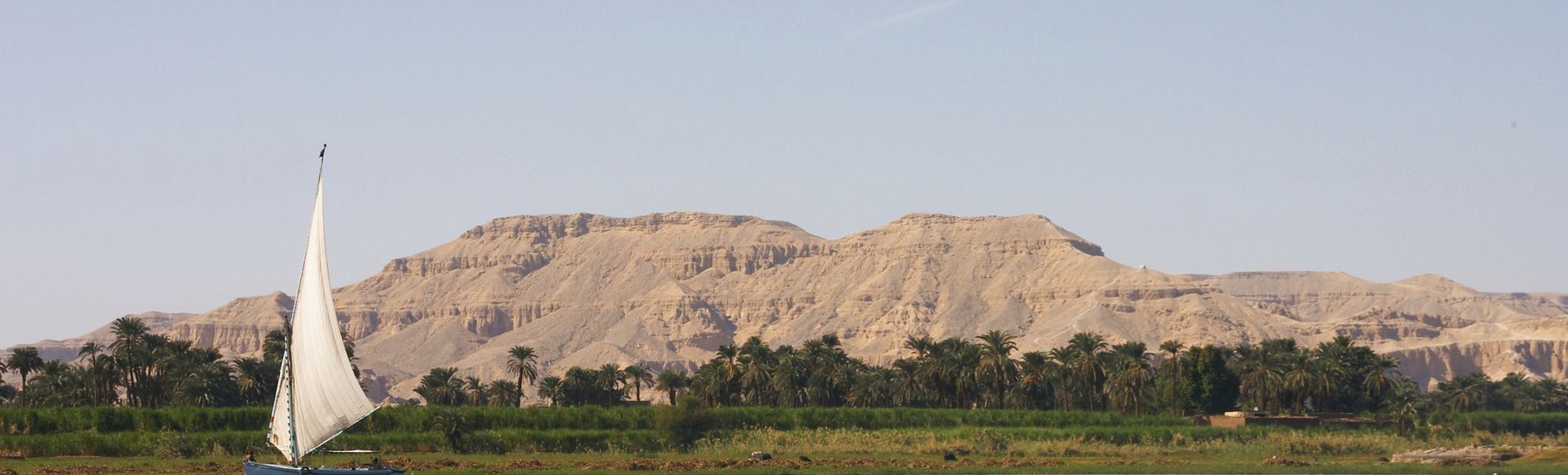 Feluke auf dem Nil vor grüner Landschaft und beeindruckendem Gebirge in Ägypten