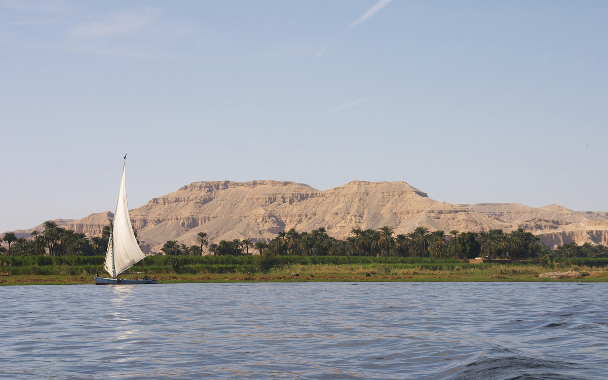 Feluke auf dem Nil vor grüner Landschaft und beeindruckendem Gebirge in Ägypten