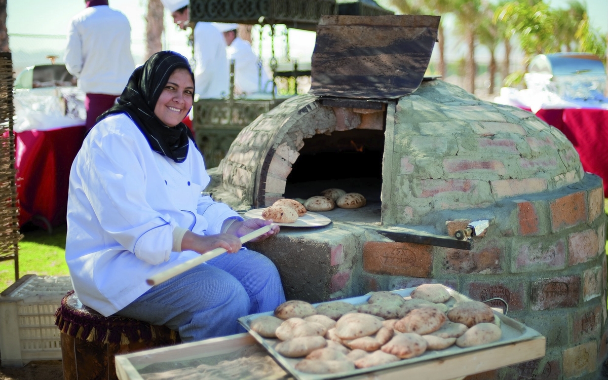 Bäckerin schiebt Brötchen in einen Steinofen auf einem Markt in Ägypten