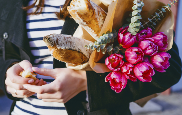 Frau mit Blumen und Baguette unterm Arm