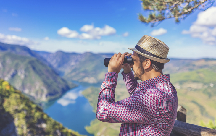 Mann mit Fernglas blickt in einen Fjord
