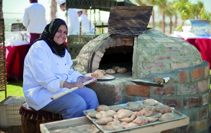 Bäckerin schiebt Brötchen in einen Steinofen auf einem Markt in Ägypten