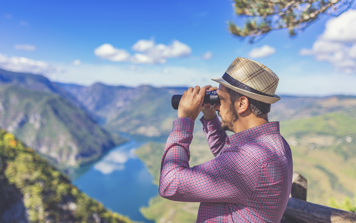 Mann mit Fernglas blickt in einen Fjord