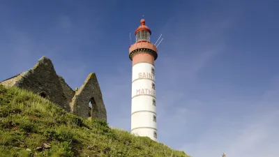 Französischer Leuchtturm auf grüner Klippe mit Blumenwiese.