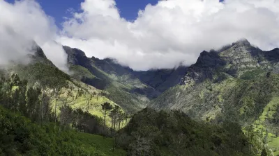 Grüne Hügel und Berge unter blauem Himmel mit Wolken.