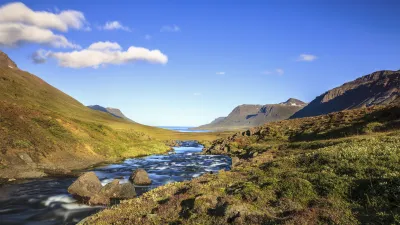 Ein Bach fließt durch eine grüne Landschaft mit Bergen im Hintergrund.