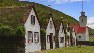 Traditionelle isländische Torfhäuser mit Grasdächern stehen an einem Hang.