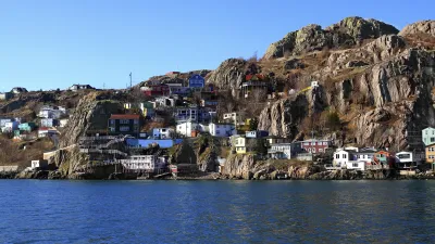 Bunte Häuser schmiegen sich an einen felsigen Hügel am Meer.