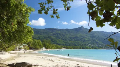 Türkisblaues Meer trifft auf weißen Sandstrand mit üppiger Vegetation.