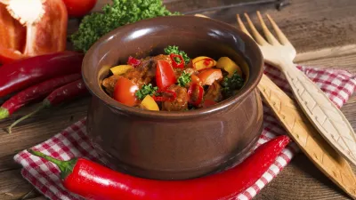 Ungarisches Gulasch in einer braunen Schüssel mit frischen Zutaten.