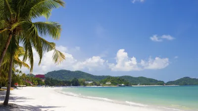 Türkisblaues Meer trifft auf weißen Sandstrand mit üppiger Vegetation.