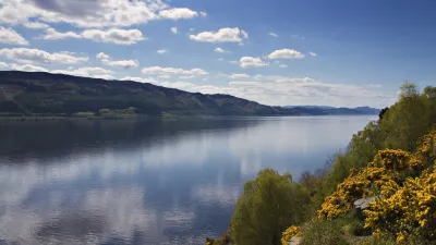 Der Loch Ness in Schottland erstreckt sich unter blauem Himmel.