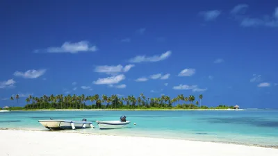 Türkisblaues Wasser umspült einen weißen Sandstrand mit Palmen.