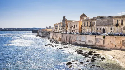 Historische Gebäude säumen die felsige Küste Siziliens am Meer.