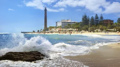 Wellen brechen am Strand von Maspalomas mit dem Leuchtturm im Hintergrund