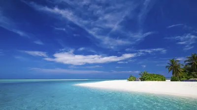 Türkisblaues Meer trifft auf weißen Sandstrand mit Palmen.