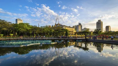 Eine belebte Uferpromenade mit Menschen und Vegetation spiegelt sich im Wasser.