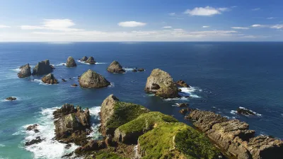 Grüne Felsen ragen aus dem blauen Meer an der Küste Neuseelands empor.