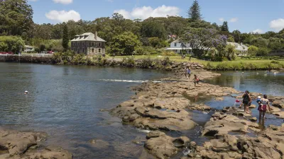 Menschen waten durch einen Fluss vor einer historischen Villa.