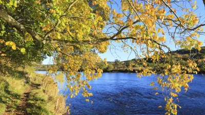 Herbstliche Bäume säumen einen ruhigen Fluss in Schottland.