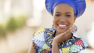 Lächelnde Zulu-Frau mit traditionellem Schmuck und Kopfbedeckung.