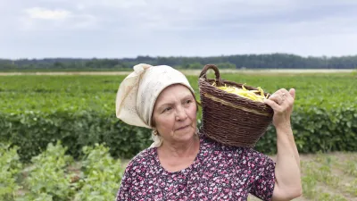 Ältere Frau trägt einen Korb mit Feldfrüchten auf dem Feld.