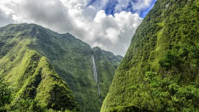 Ein hoher Wasserfall stürzt zwischen grünen Berghängen herab.