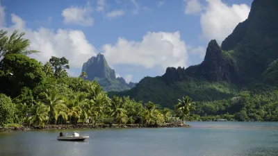Boot fährt an üppiger Küstenlandschaft mit Bergen in Moorea, Französisch-Polynesien.