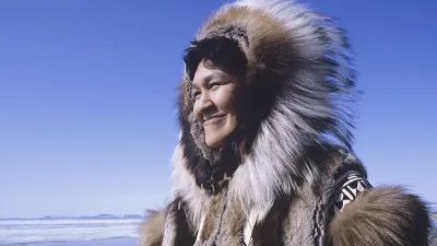 Lachende Inuit-Frau mit traditioneller Winterbekleidung im Schnee.
