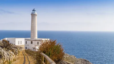 Weißer Leuchtturm steht auf felsiger Küste mit Blick aufs Meer.