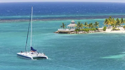 Katamaran segelt vor der Küste Jamaikas mit Palmen und Strand