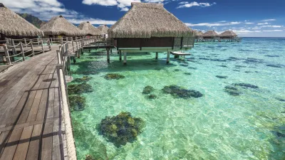 Tropische Hütten stehen auf Stelzen in einem klaren, türkisfarbenen Wasser.