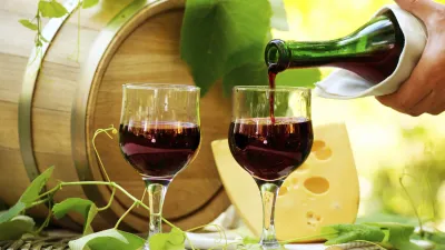 Rotwein wird in Gläser gegossen, neben Käse und einem Weinfass.
