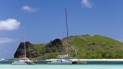 Zwei Katamarane ankern vor einer grünen Insel im türkisfarbenen Meer.