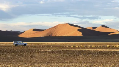 Ein weißes Auto fährt durch die namibische Wüstenlandschaft.
