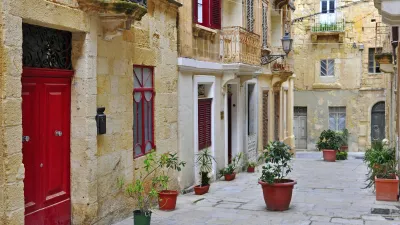 Rote Tür in einer gepflasterten Gasse mit blühenden Töpfen