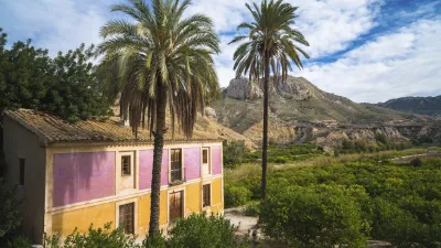 Ein farbenfrohes Haus steht in einem grünen Tal mit Bergen im Hintergrund.
