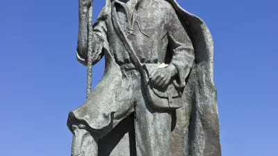 Pilgerstatue mit Wanderstab auf einem Felsen