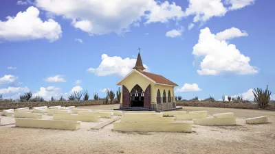 Eine kleine gelbe Kapelle steht inmitten einer kargen Landschaft.