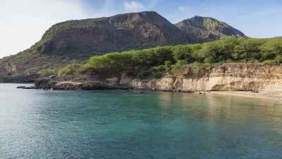 Türkisblaues Meer trifft auf grüne Hügel und einen Sandstrand.