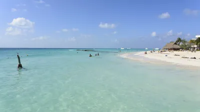 Türkisblaues Meer trifft auf weißen Sandstrand mit badenden Menschen.