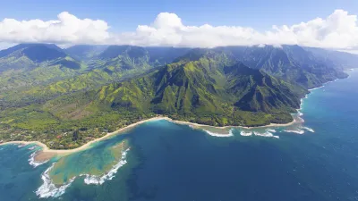 Grüne Küstenlinie mit Strand und Wellen unter blauem Himmel.