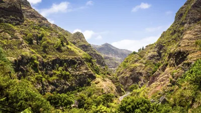 Grüne Berghänge und eine kurvenreiche Straße in einer tiefen Schlucht.