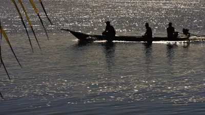 Ein Boot mit drei Personen gleitet auf dem Wasser unter dem Abendhimmel.