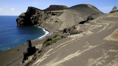 Vulkanlandschaft mit schwarzem Sandstrand und Hügeln am Meer.