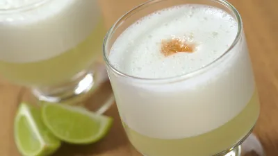 Pisco Sour Cocktail mit Limettenspalten auf Holzoberfläche