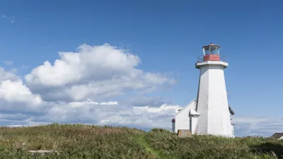 Weißer Leuchtturm steht auf grüner Wiese unter blauem Himmel.