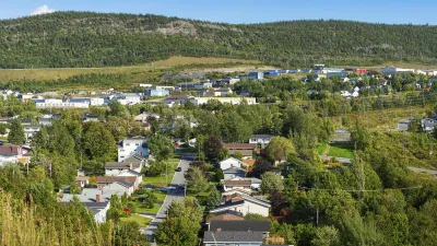 Panoramablick auf eine Stadt mit Häusern und grünen Hügeln im Hintergrund.