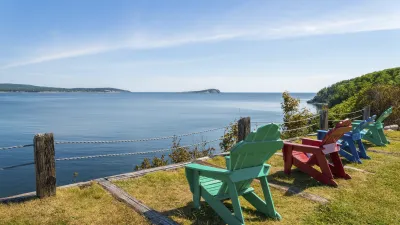 Bunte Adirondack-Stühle stehen auf einer grünen Wiese mit Blick auf das Meer.