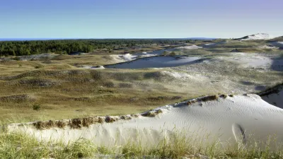 Sanddünen erstrecken sich bis zum Horizont mit spärlicher Vegetation.